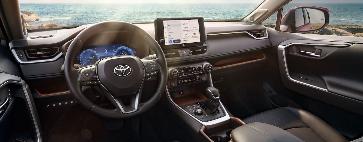 The black interior of a 2024 Toyota RAV4 is shown from the driver's seat.