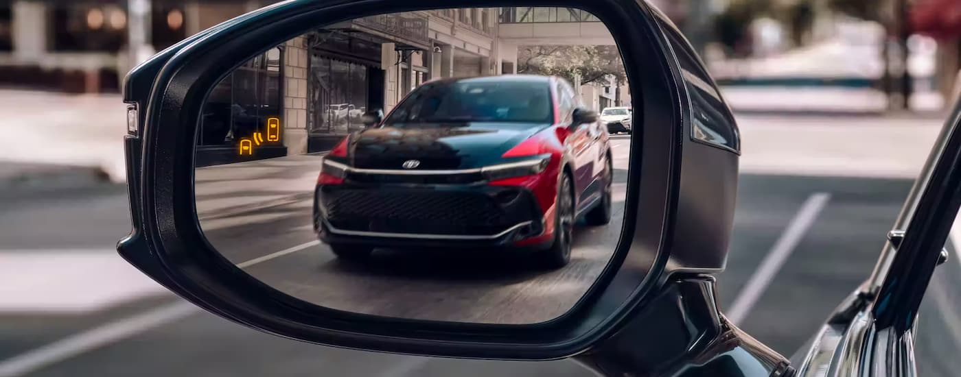 A red and black 2023 Toyota Crown is shown in the rear view mirror of a vehicle driving on a street.