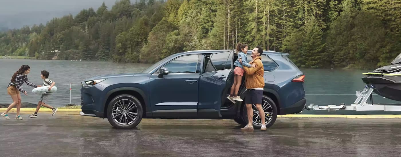 A blue 2024 Toyota Grand Highlander is shown from the side parked near a lake.