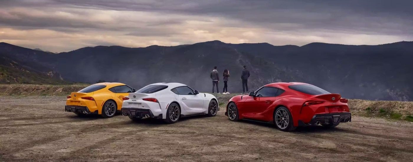 A yellow, a white, and a red 2022 Toyota GR Supra are shown from behind overlooking distant mountains.
