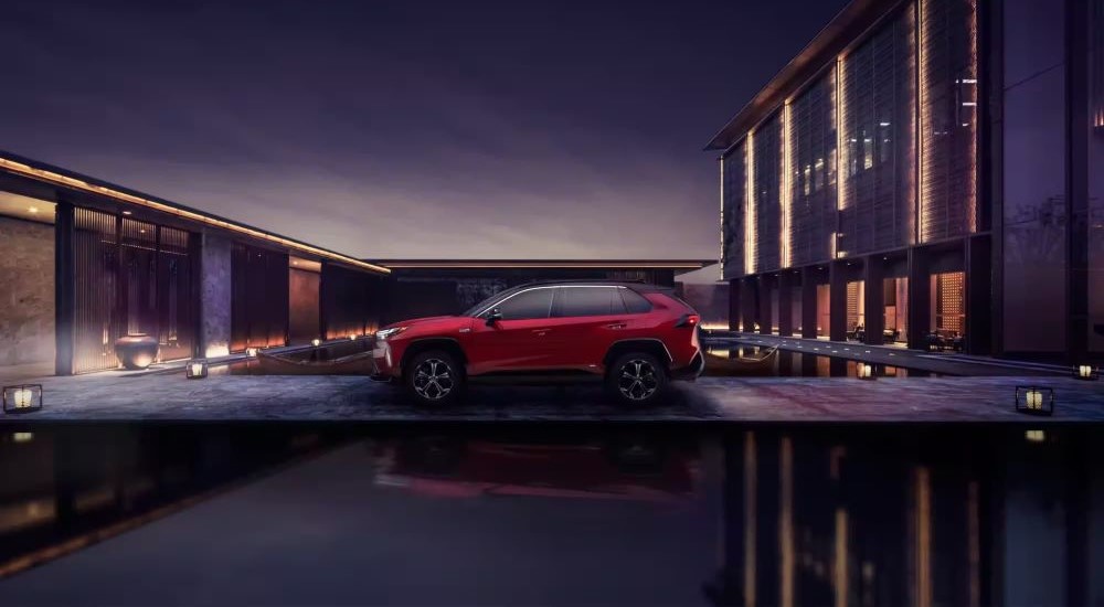 A red 2023 Toyota RAV4 Prime is shown on a modern driveway at night.