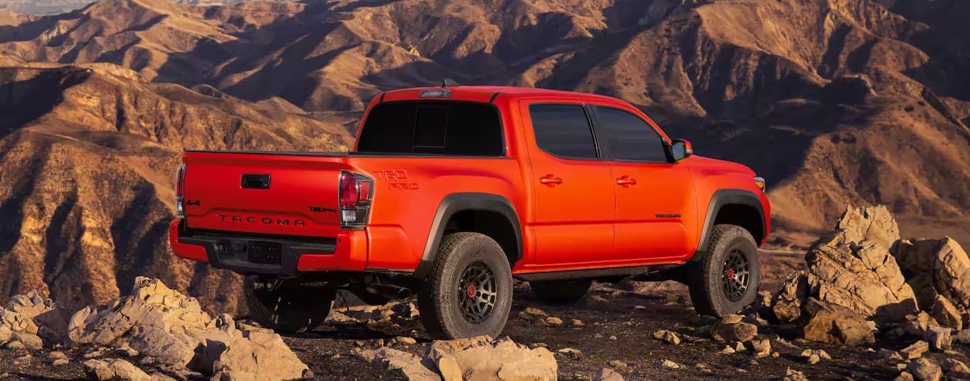 An orange 2023 Toyota Tacoma TRD Pro is shown from the rear parked in a rocky mountain area.