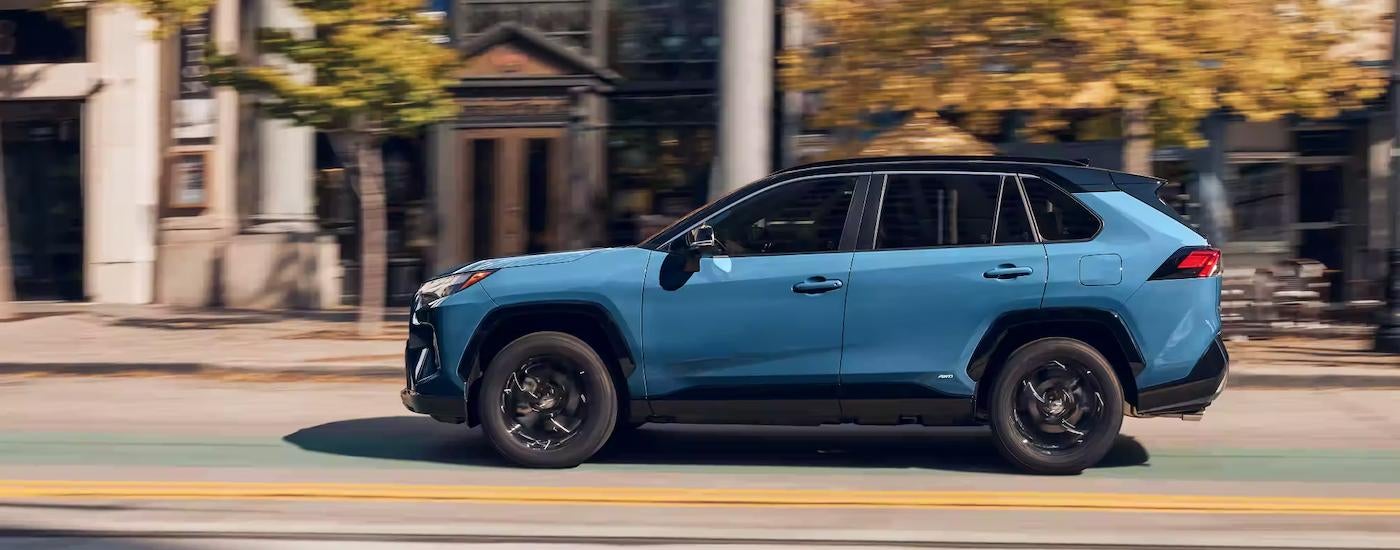A blue 2023 Toyota RAV4 XSE is shown from the side driving on a city street.